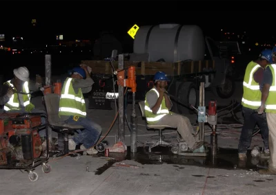 Workers in row drilling cores in concrete at night