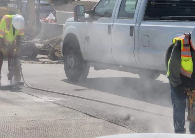 Workers using pneumatic hammer drills on roadway by truck