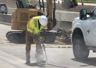 Worker using pneumatic hammer drill on roadway