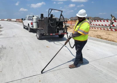 Worker injecting sealant into concrete joint with sealer trailer