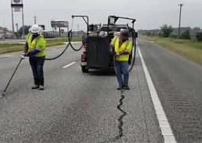 Workers injecting sealant in roadway cracks and gaps